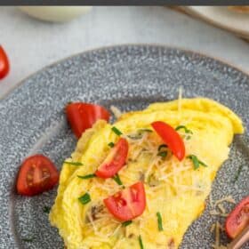a fluffy air fryer omelet topped with sliced tomatoes, cheese, and parsley on a grey plate.