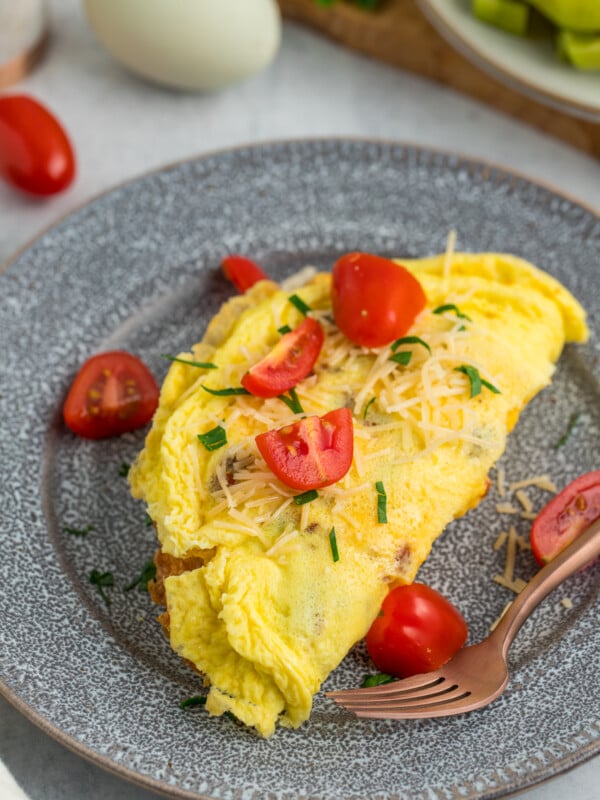 a fluffy air fryer omelet topped with sliced tomatoes, cheese, and parsley on a grey plate.