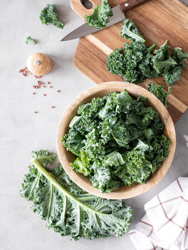 a wooden bowl full of chopped kale, and a wooden cutting board with a knife.