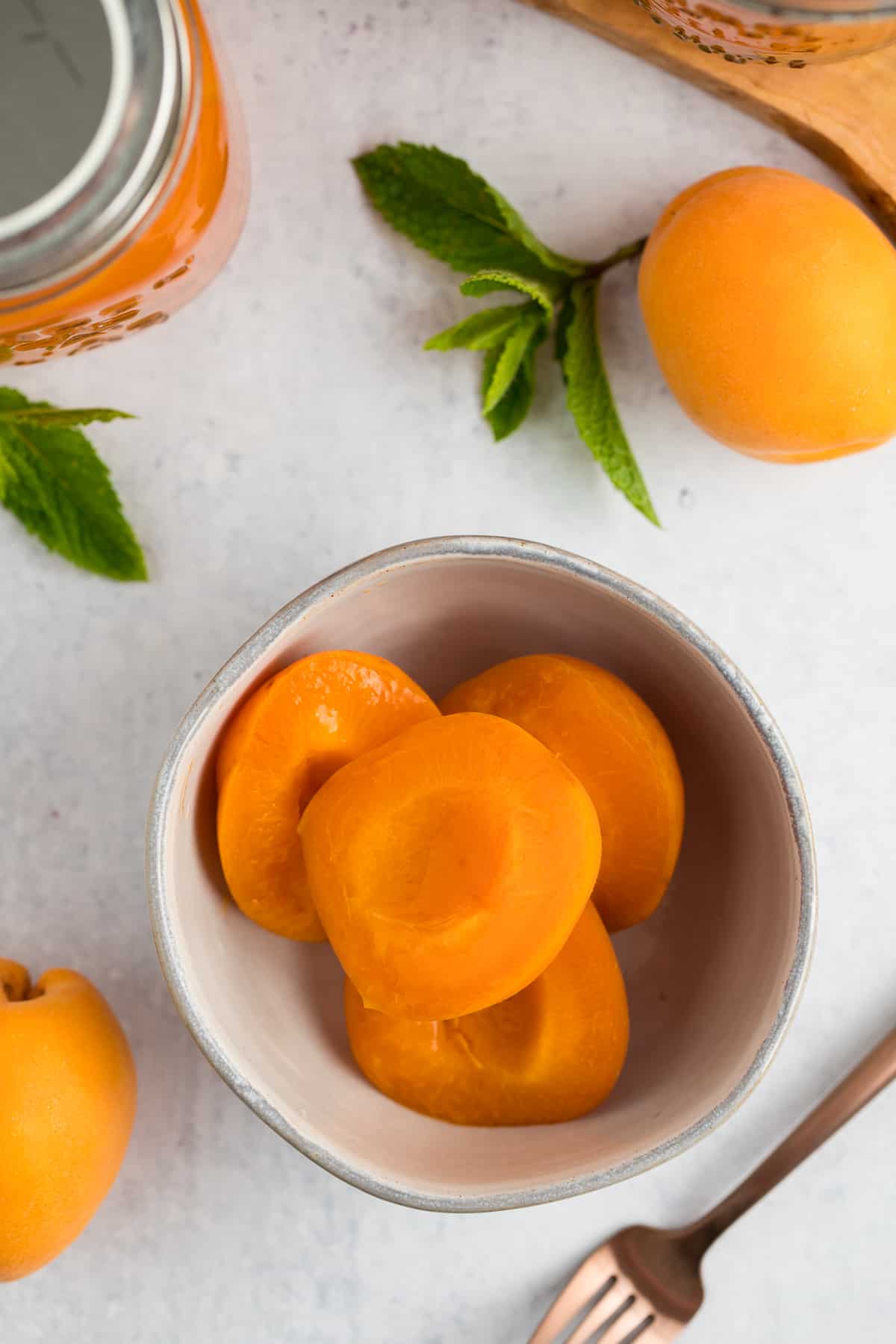 sliced apricots in a grey bowl with mint and a fork.
