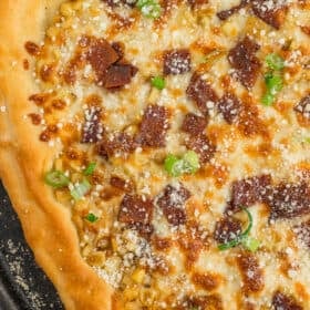 homemade corn pizza on a cast iron pizza stone topped with Parmesan, bacon, and sliced green onions.