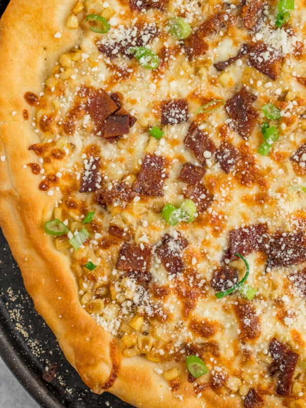 homemade corn pizza on a cast iron pizza stone topped with Parmesan, bacon, and sliced green onions.