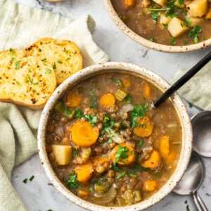 two bowls of Instant Pot lentil soup topped with parsley and a bowl of garlic bread.