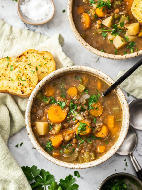 two bowls of Instant Pot lentil soup topped with parsley and a bowl of garlic bread.