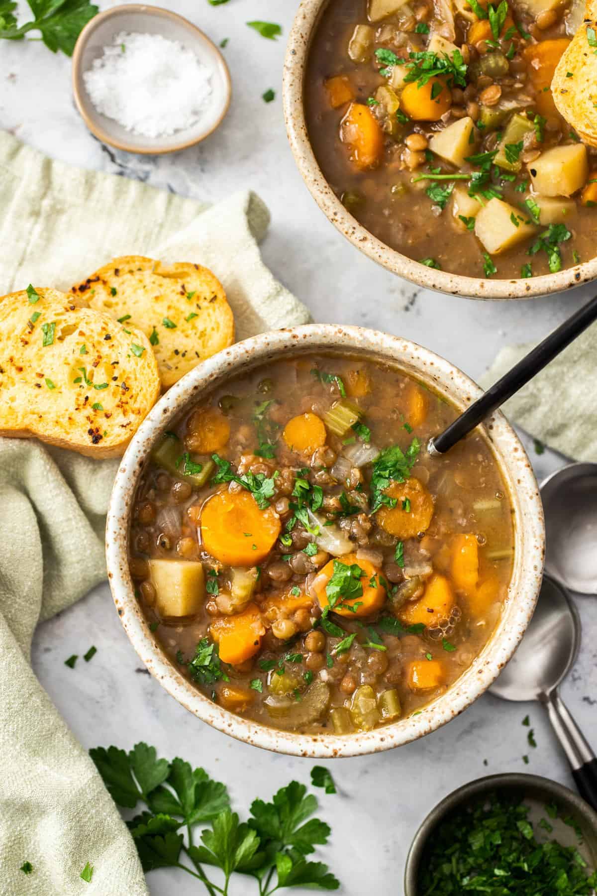 two bowls of Instant Pot lentil soup topped with parsley and a bowl of garlic bread.