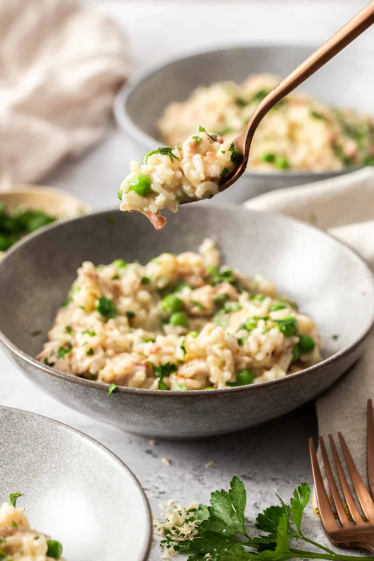 a forkful of chicken and pea risotto over a grey bowl.