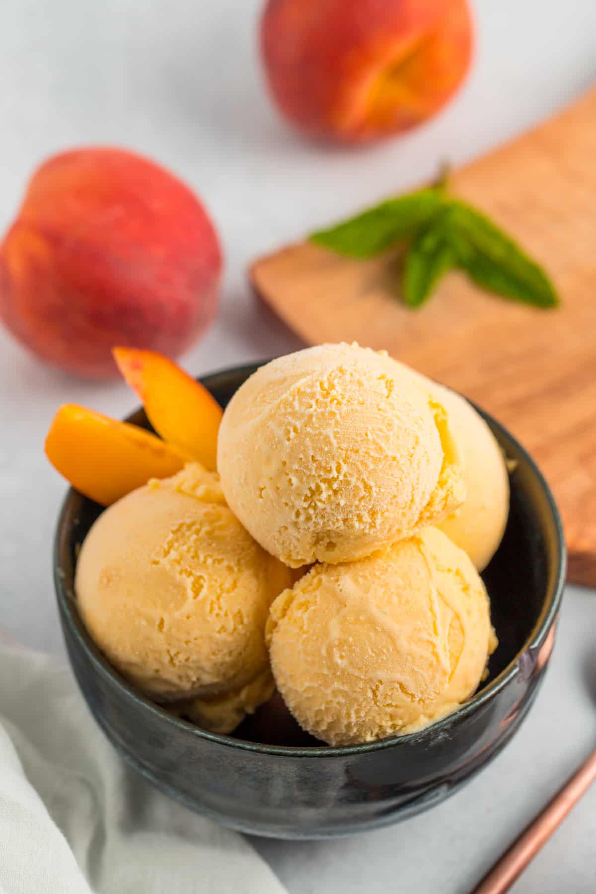 a blue bowl with multiple scoops of homemade peach ice cream, with whole peaches.