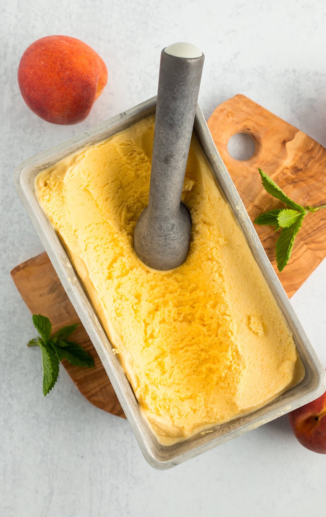 a metal loaf pan with peach ice cream and an ice cream scoop.