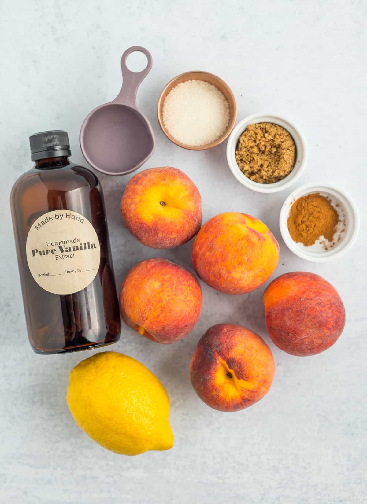 Peaches, vanilla, 2 bowls of sugar, a bowl of cinnamon, and a lemon on a white board.