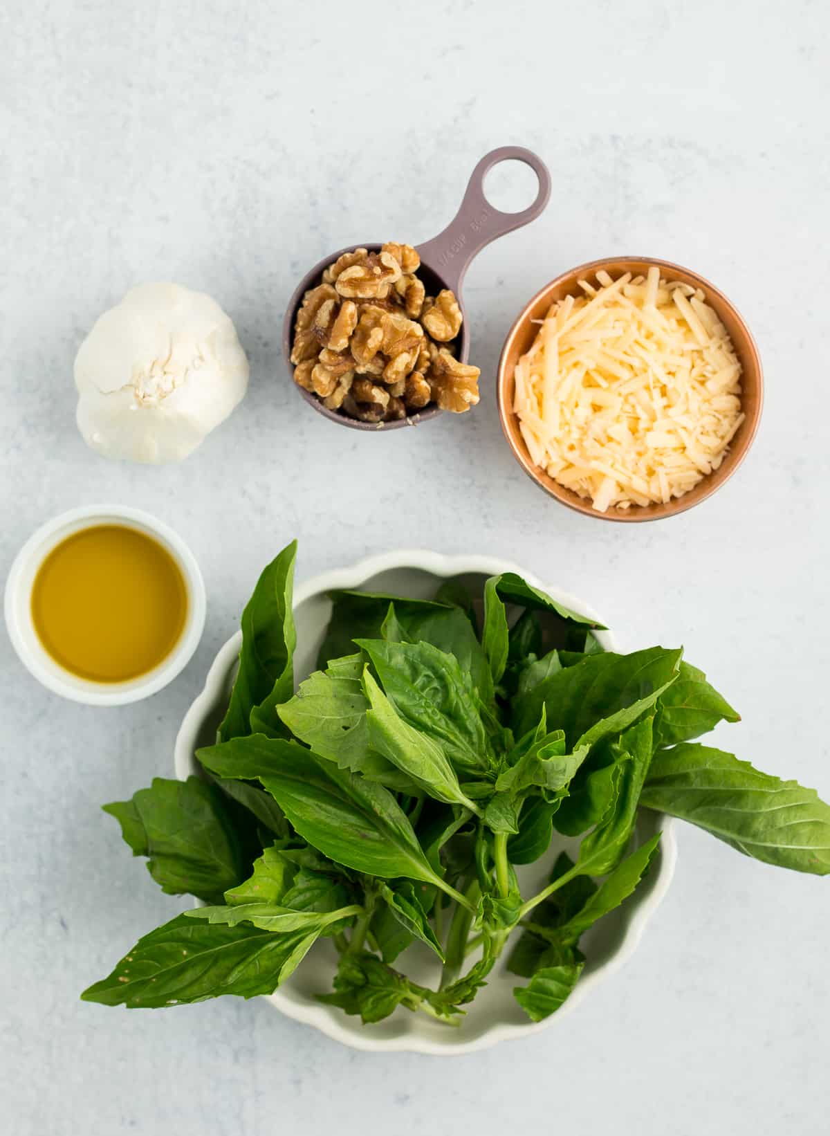 basil, Parmesan cheese, walnuts, garlic, and olive oil on a grey board.