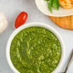 a white bowl with pine nut free pesto, tomatoes, and bread sticks.