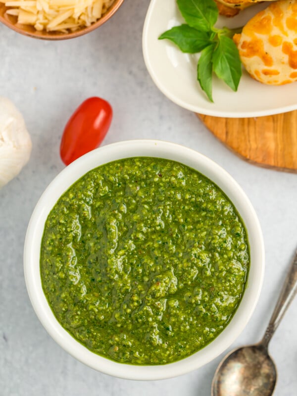 a white bowl with pine nut free pesto, tomatoes, and bread sticks.