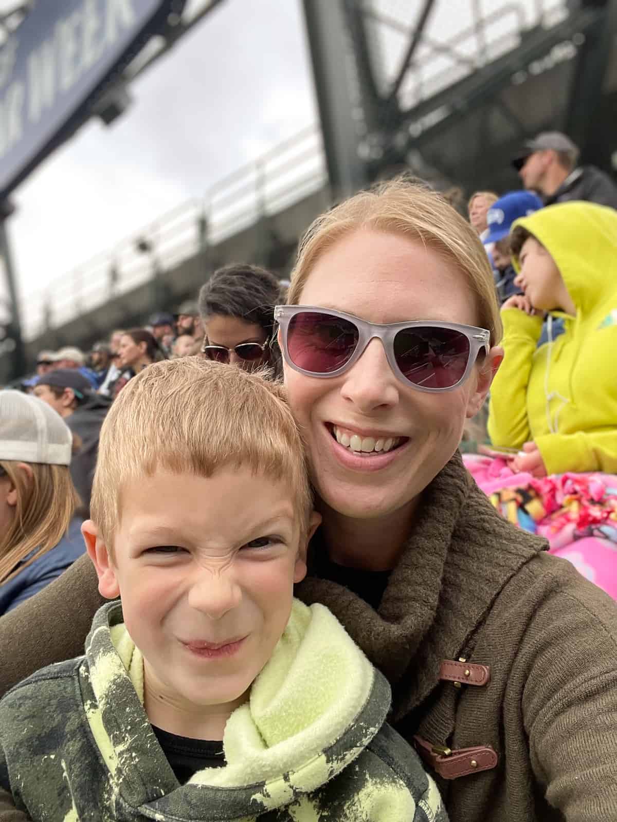 a mom and her son who has a silly looking smile at a ballpark.