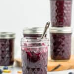 5 jars of blueberry rhubarb jam, one is opened with a spoon sticking out of it.