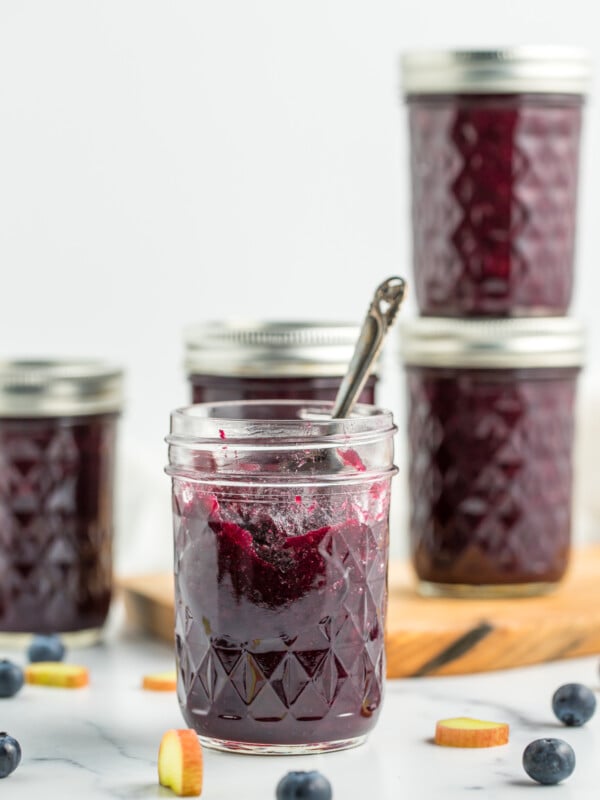 5 jars of blueberry rhubarb jam, one is opened with a spoon sticking out of it.