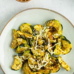 a grey plate with sliced roasted air fryer zucchini topped with Parmesan.