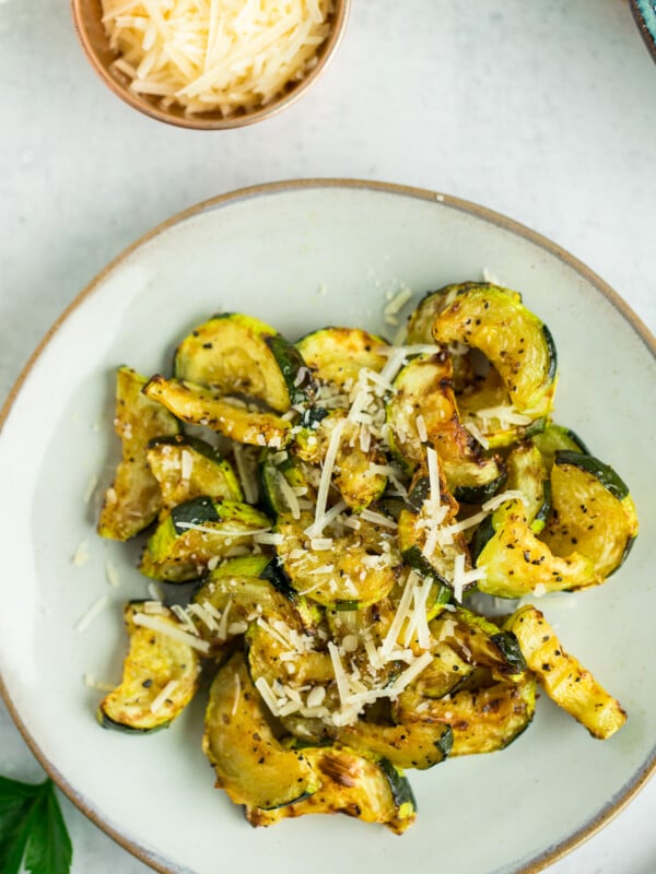 a grey plate with sliced roasted air fryer zucchini topped with Parmesan.