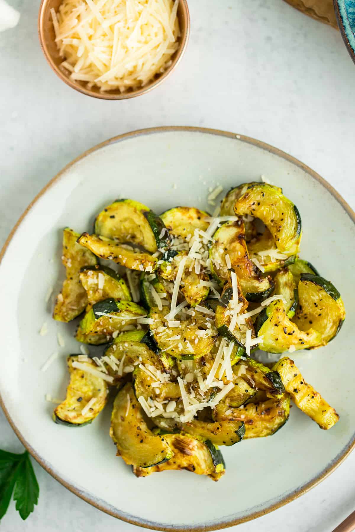 a grey plate with sliced roasted air fryer zucchini topped with Parmesan.
