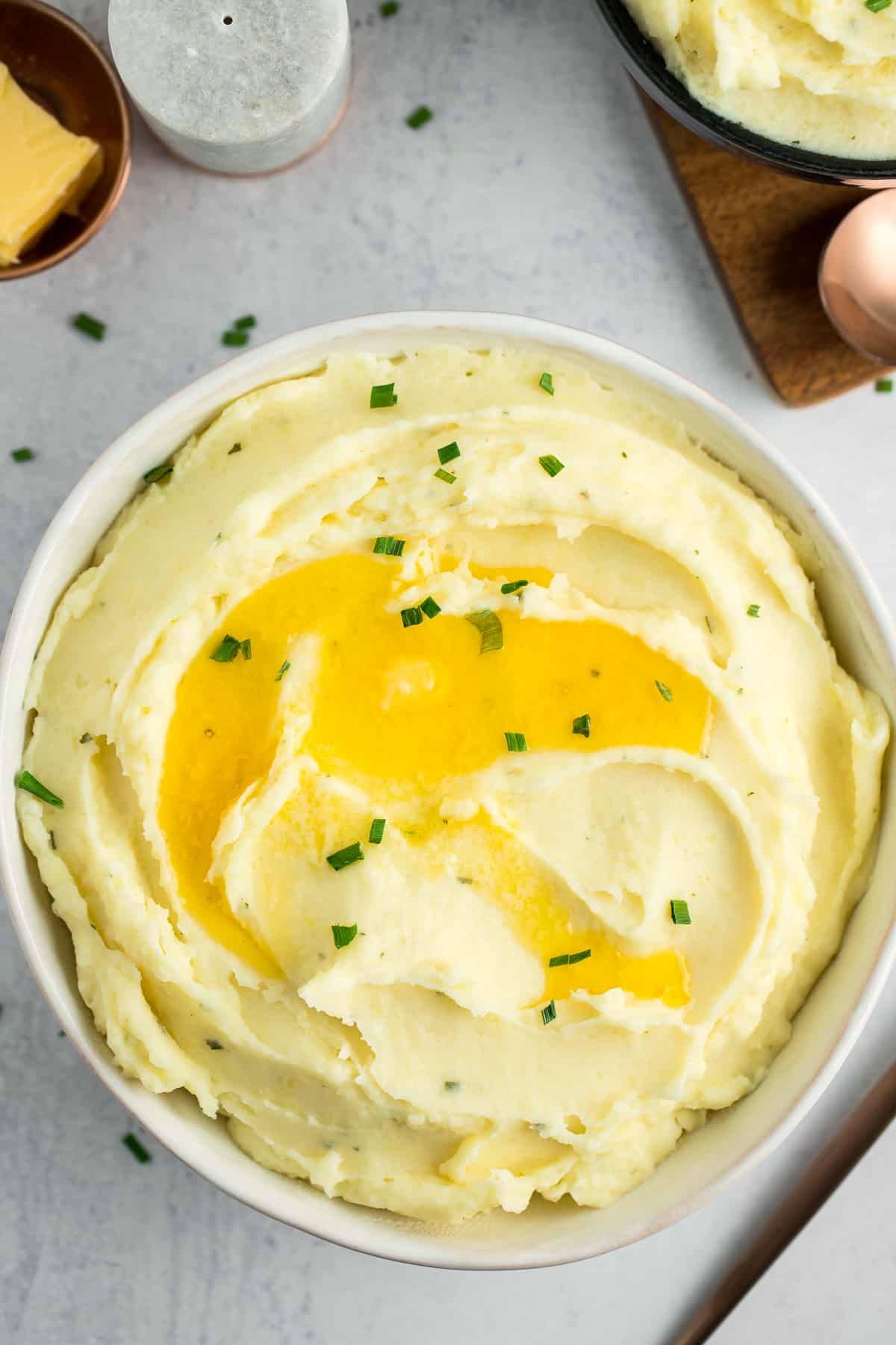 a white bowl of Boursin mashed potatoes topped with melting butter and chopped chives.