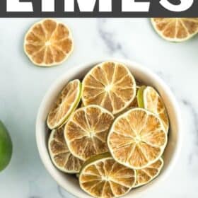 a white bowl of dried lime slices on a marble board with whole and halved limes.