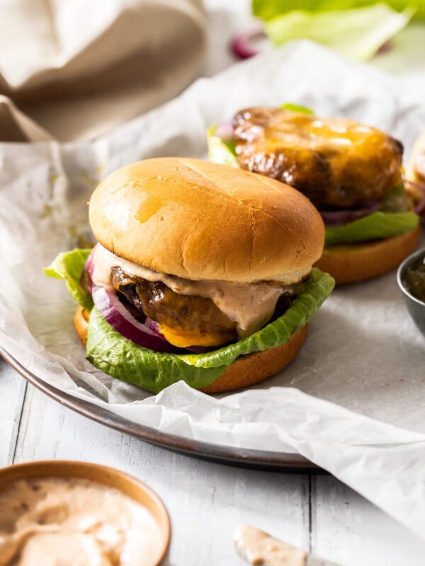 a close up of an air fryer turkey burger with lettuce, cheese, and onion and another turkey burger behind it without a top bun.