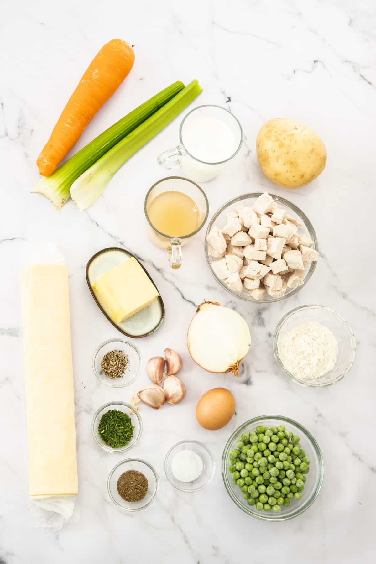 a bowl of frozen peas, carrots, celery, turkey, butter, and other ingredients on a white board.