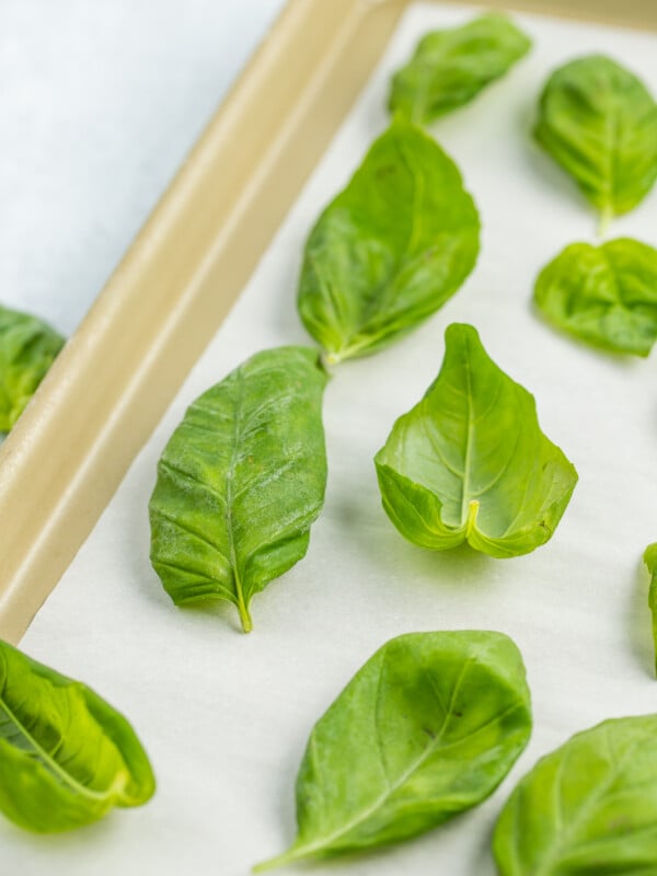 frozen basil leaves on a gold baking sheet lined with parchment.