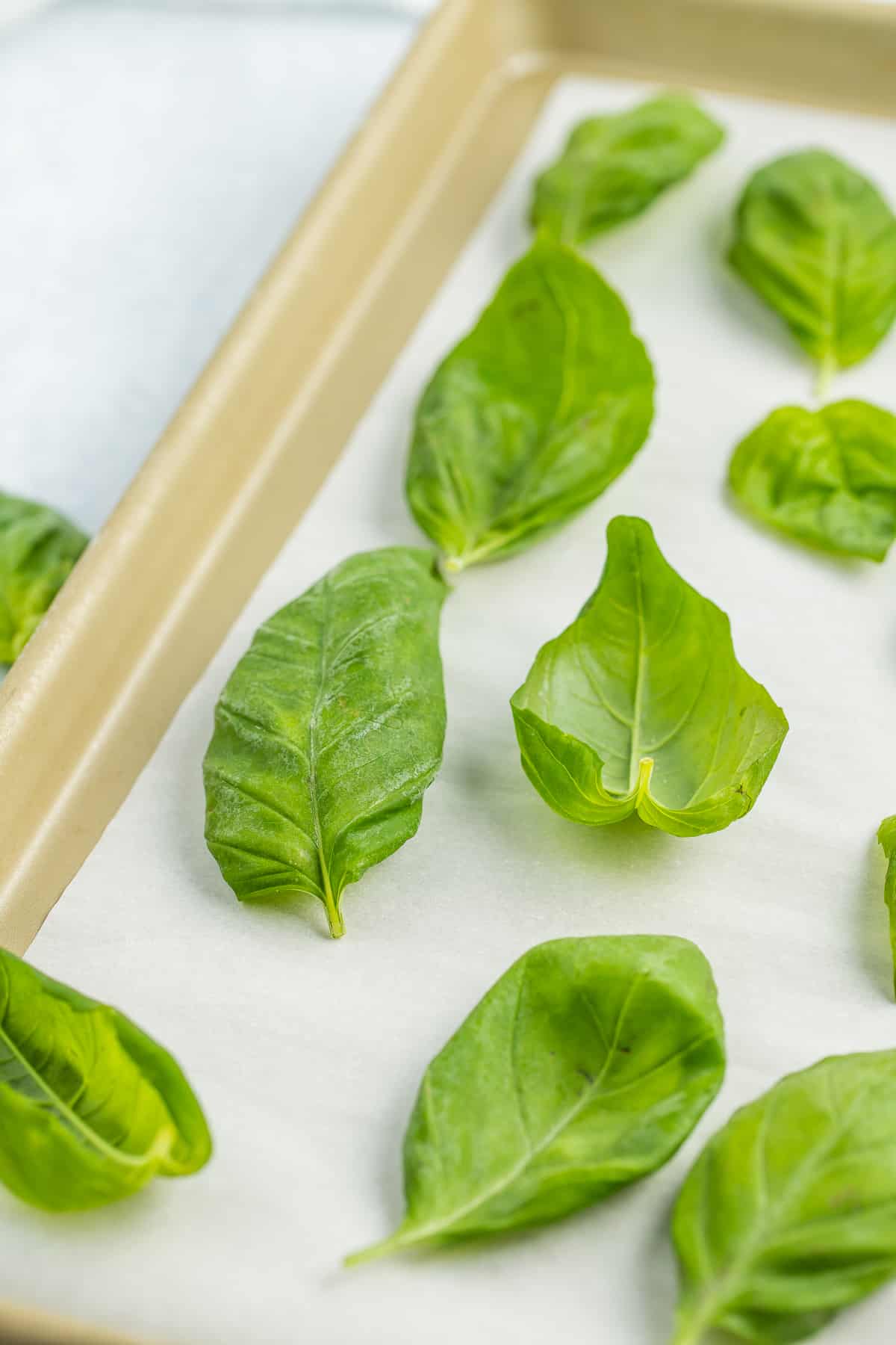 frozen basil leaves on a gold baking sheet lined with parchment.