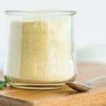 a small glass dish of homemade garlic powder on a small wooden cutting board.