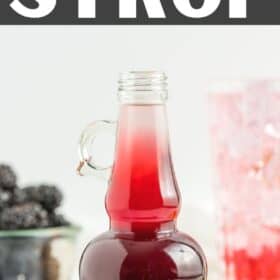 a glass bottle of blackberry simple syrup with a glass of syrup and sparkling water with a gold straw.