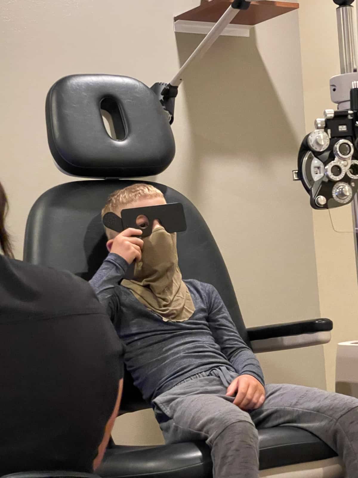 a kid in an eye exam chair with a mask