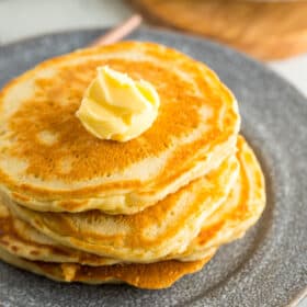 4 sour cream pancakes stacked on a grey plate with a small pat of butter.