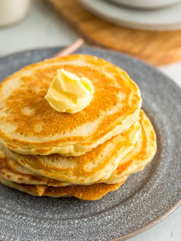 4 sour cream pancakes stacked on a grey plate with a small pat of butter.