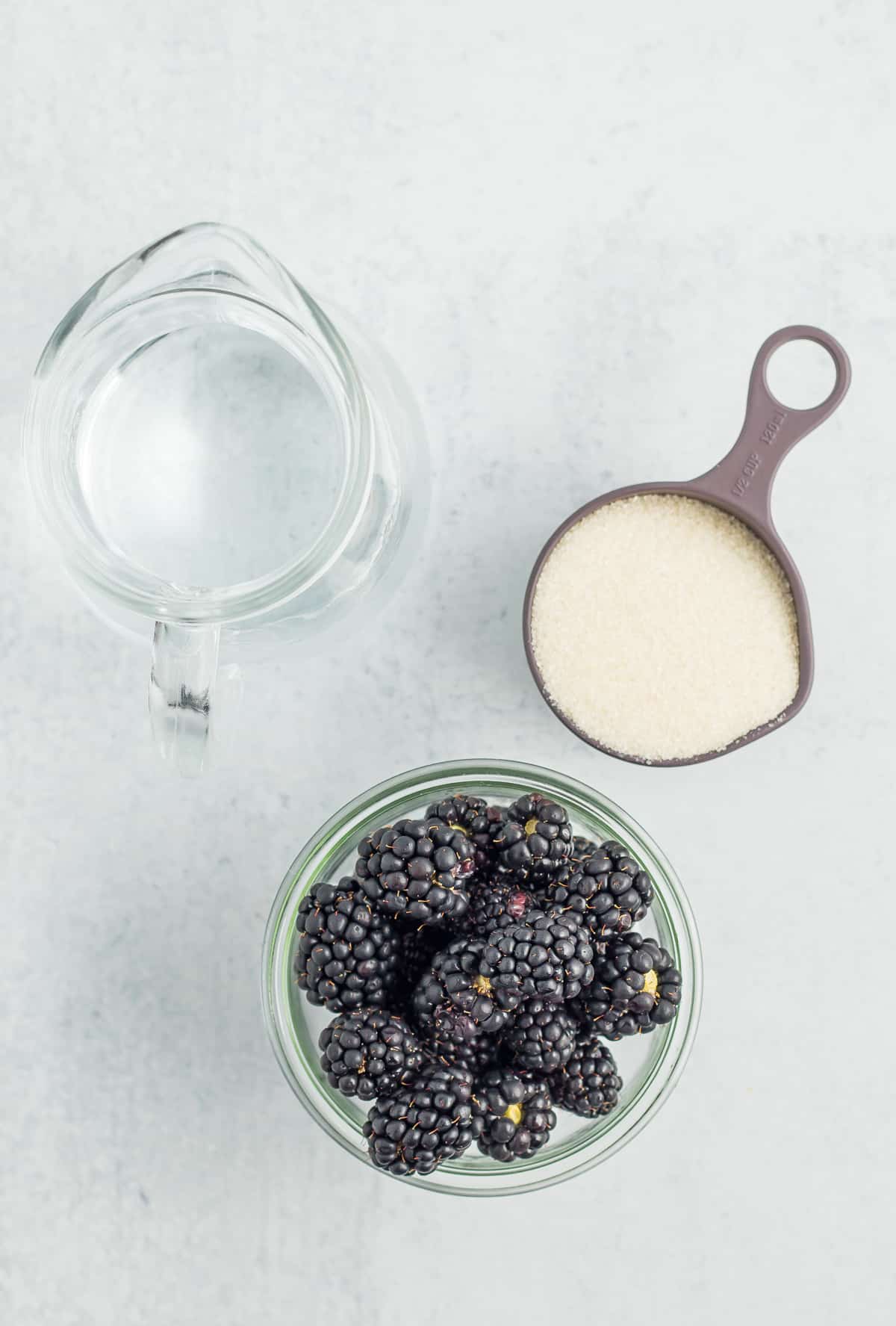 a pitcher of water, a measuring cup of sugar, and a bowl of blackberries.