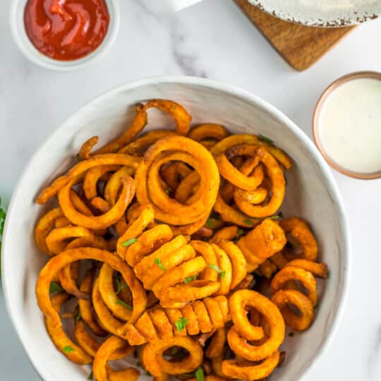 a white bowl with air fried curly fries with 2 bowls of dipping sauce.