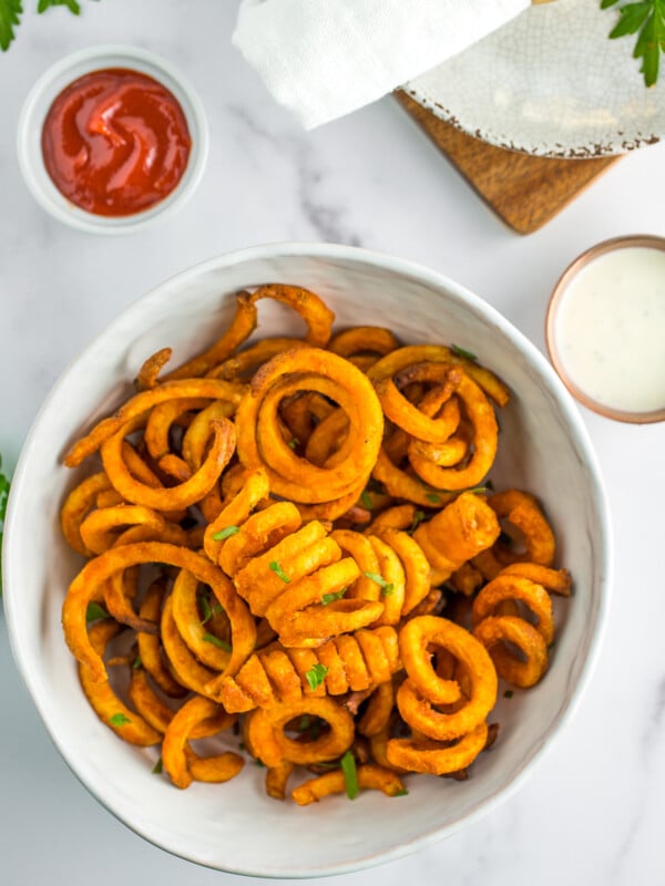 a white bowl with air fried curly fries with 2 bowls of dipping sauce.
