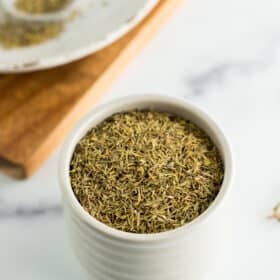 a small grey dish filled with dehydrated thyme on a white board.