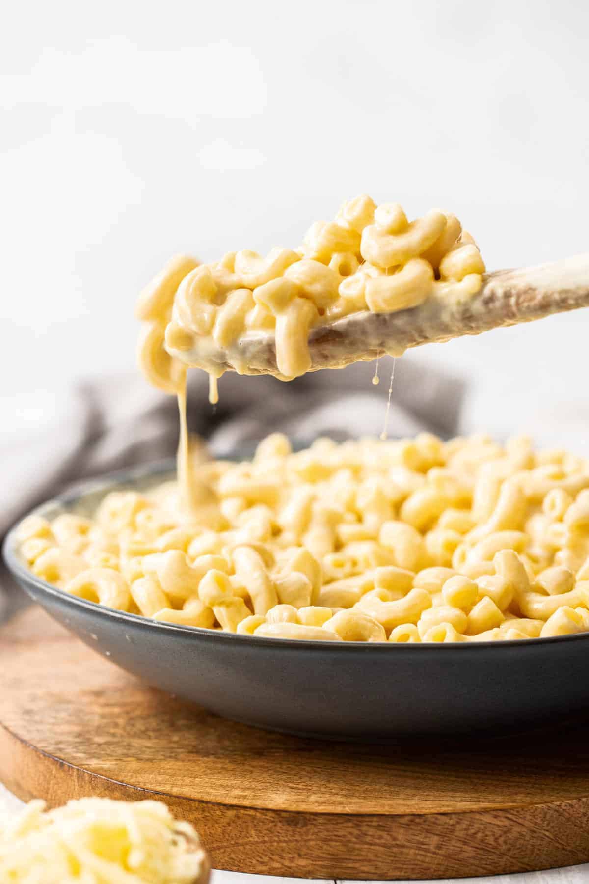 a wooden spoon lifting up a serving of Instant Pot mac and cheese out of a black bowl.