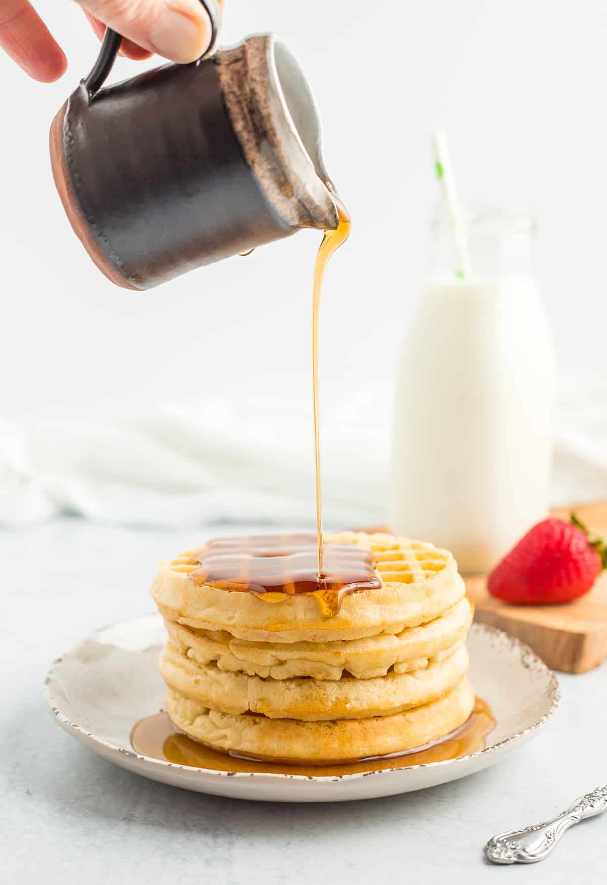 maple syrup being poured over a stack of waffles.