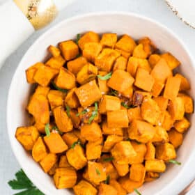 a white bowl with roasted sweet potatoes topped with flaky sea salt and chopped parsley.