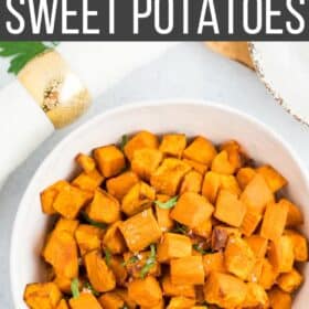 a white bowl with roasted sweet potatoes topped with flaky sea salt and chopped parsley.