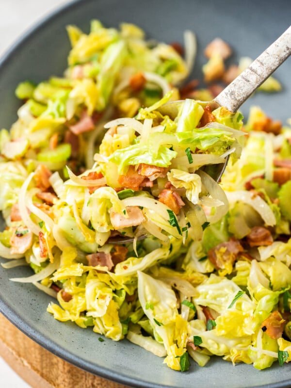 a grey bowl with bacon fried cabbage and a fork.