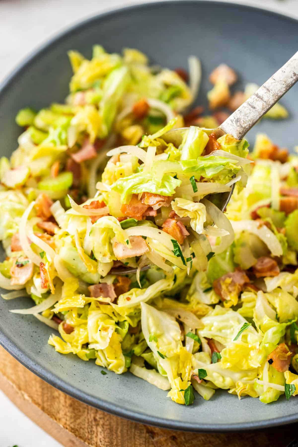 a grey bowl with bacon fried cabbage and a fork.