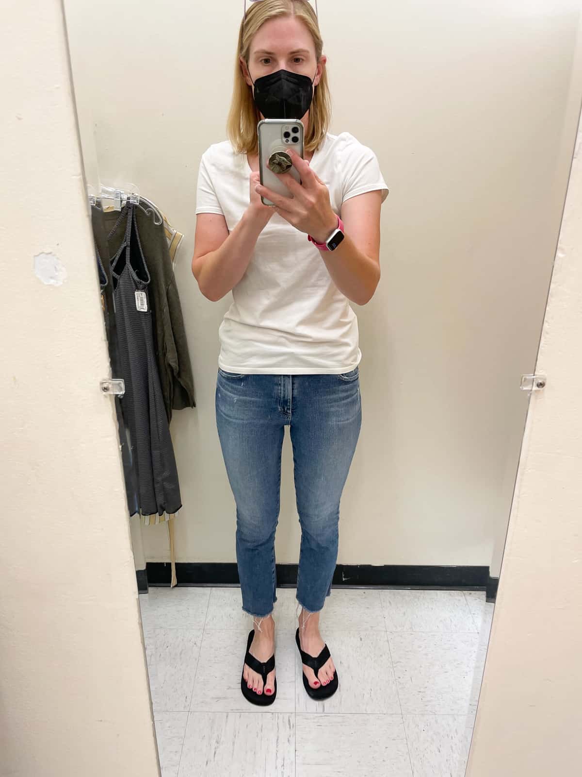 a woman in a black mask, white tshirt, and cropped jeans in a changing room.