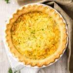 a whole quiche topped with dill on a wooden board.