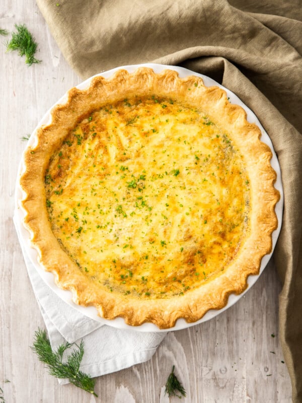 a whole quiche topped with dill on a wooden board.