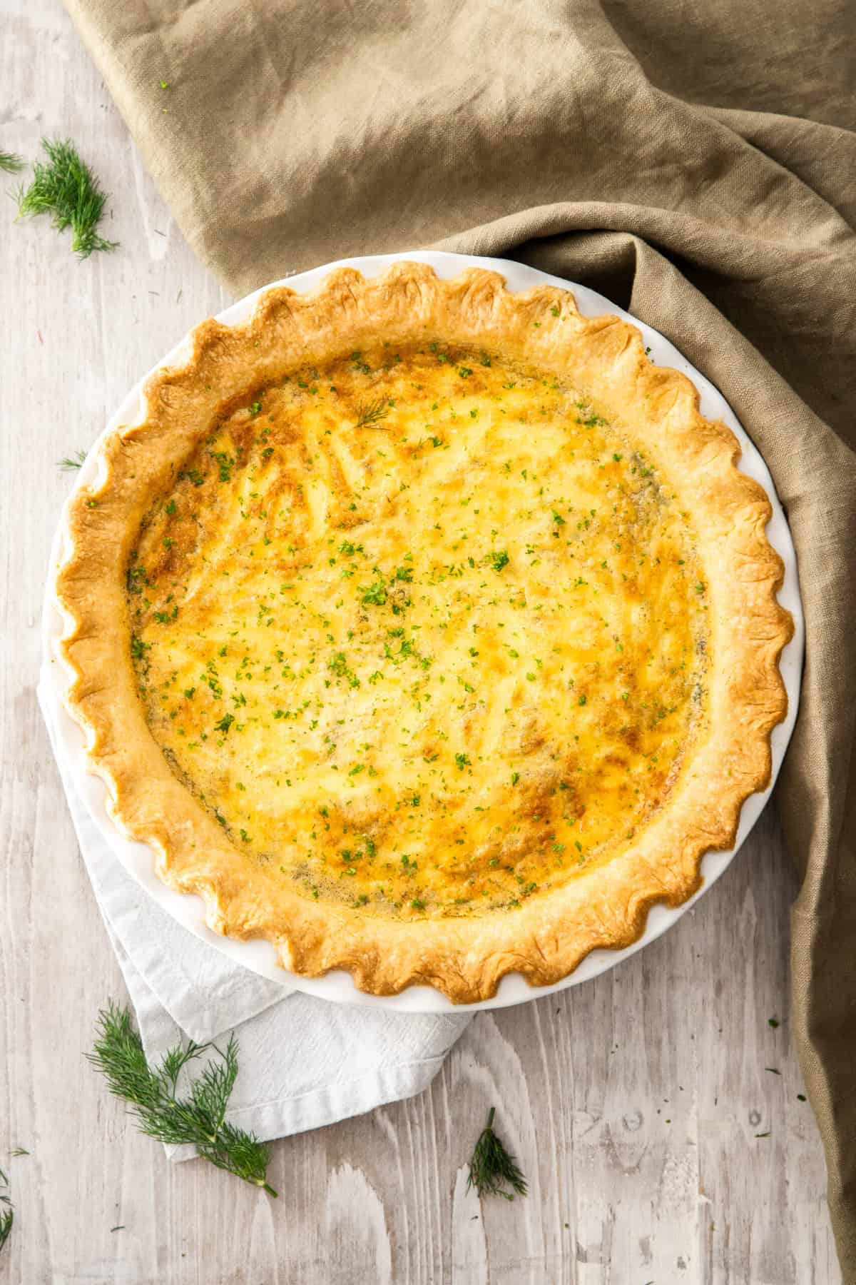 a whole quiche topped with dill on a wooden board.