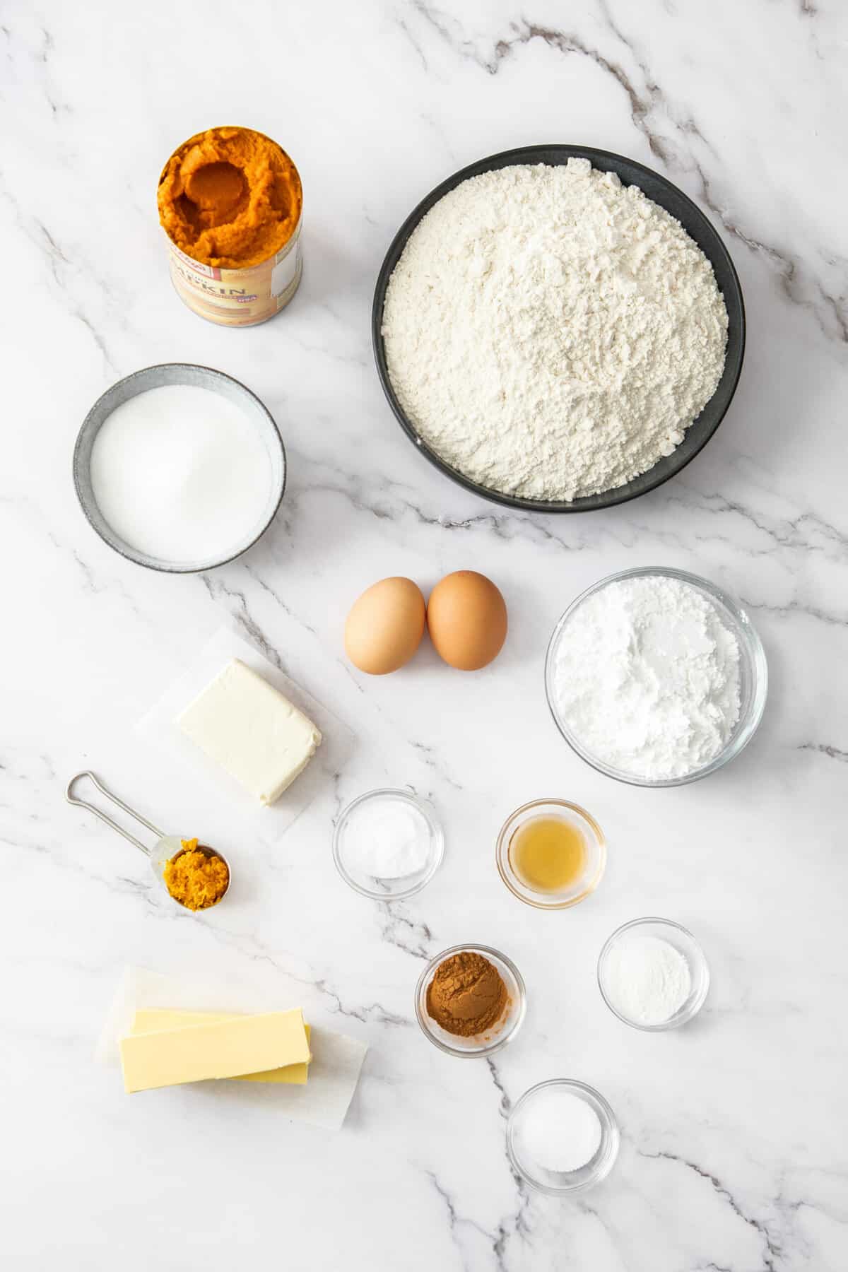 flour, eggs, butter, vanilla, a can of pumpkin puree and other ingredients on a white board.