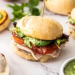a sandwich with turkey, tomato, bacon, and pesto on a white board with condiments and lettuce.