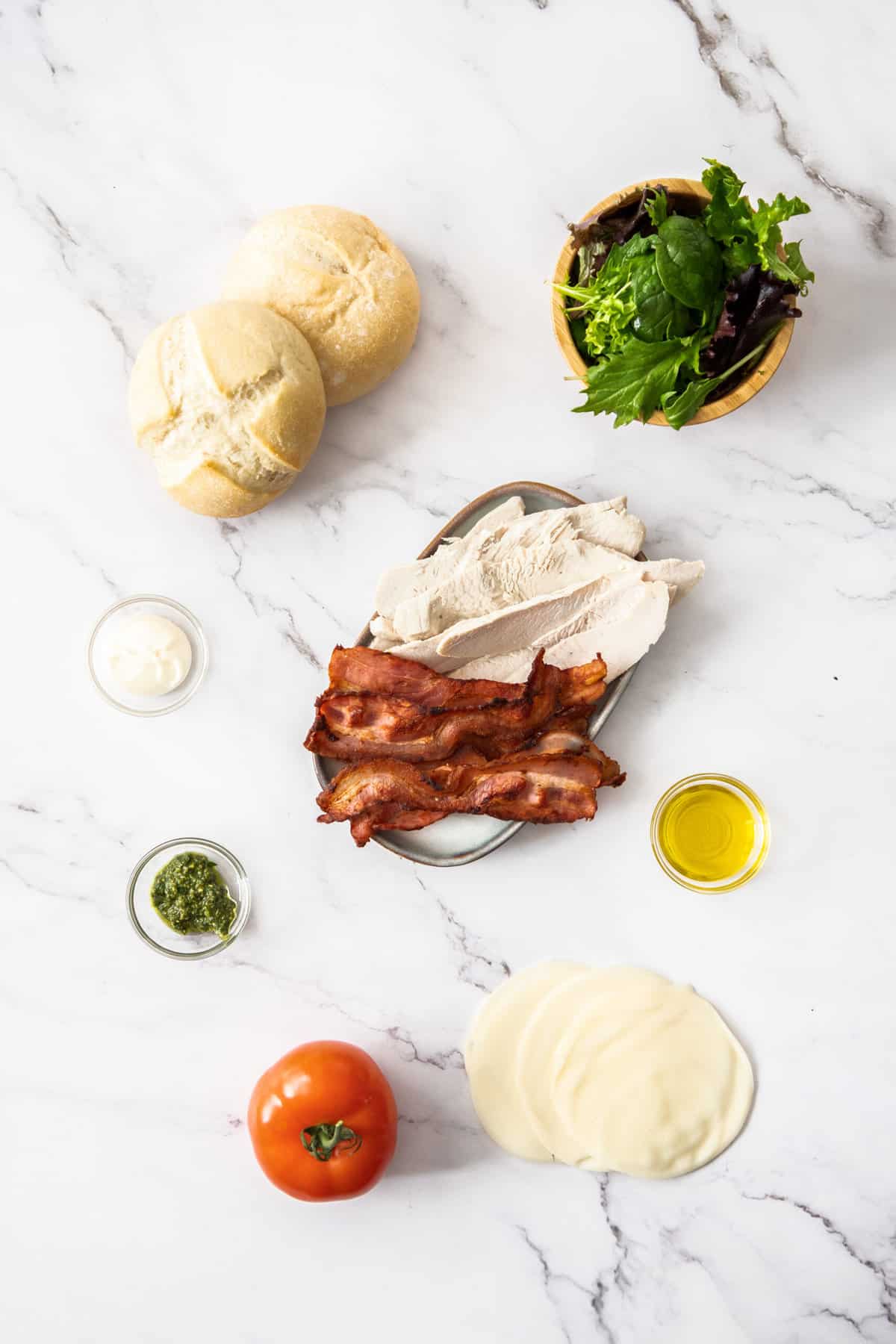 rolls, greens, tomato, cheese, turkey, bacon, and other ingredients on a white board.